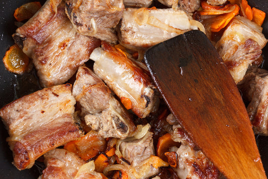 Searing oxtail with carrots in a pan with a wooden spatula.