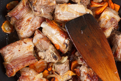 Searing oxtail with carrots in a pan with a wooden spatula.