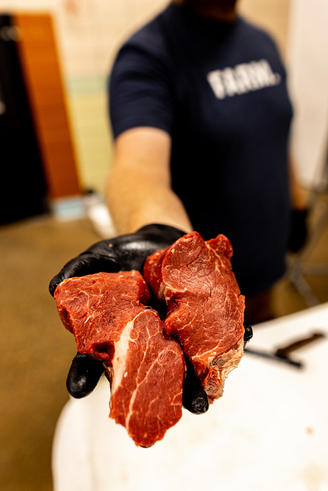 Person holding raw meat with black gloves in a kitchen setting