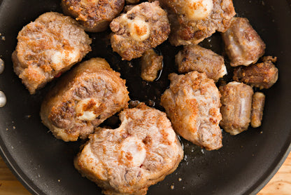 Browned oxtail pieces in a black pan on a wooden surface