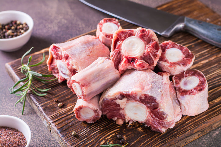 Raw oxtail on a wooden cutting board with a knife and seasonings in the background.