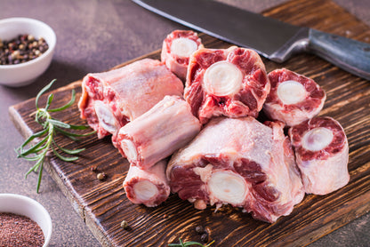 Raw oxtail on a wooden cutting board with a knife and seasonings in the background.