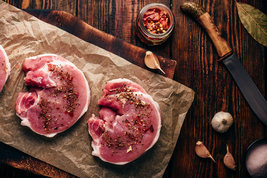 Raw pork chops seasoned with spices on a wooden cutting board with a knife and spices.