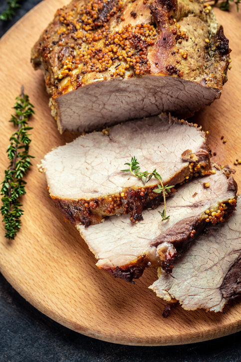 Sliced roasted pork on a wooden plate with thyme garnish
