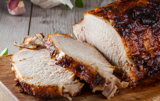Sliced roasted pork tenderloin on a wooden cutting board with a rustic background.