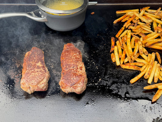 Two pieces of cooked meat on a grill with fries and a strainer of sauce nearby.